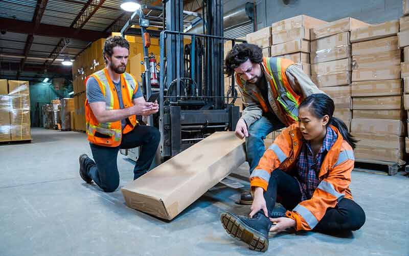 Injured warehouse worker receiving help after a workplace accident, before seeking workers compensation benefits.