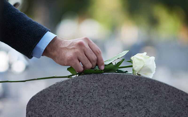 White rose being placed on a gravestone in remembrance of a loved one's wrongful death.