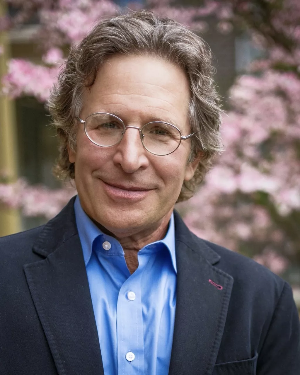 Steven M Schoenfeld's headshot in front of pink flowering trees.