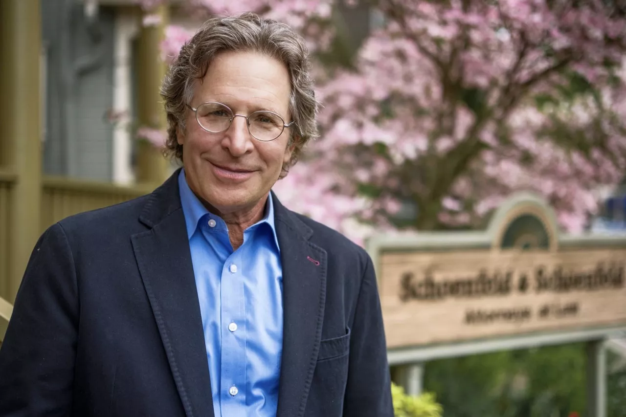 Steven M. Schoenfeld standing outside his law office with a flowering tree in the background.