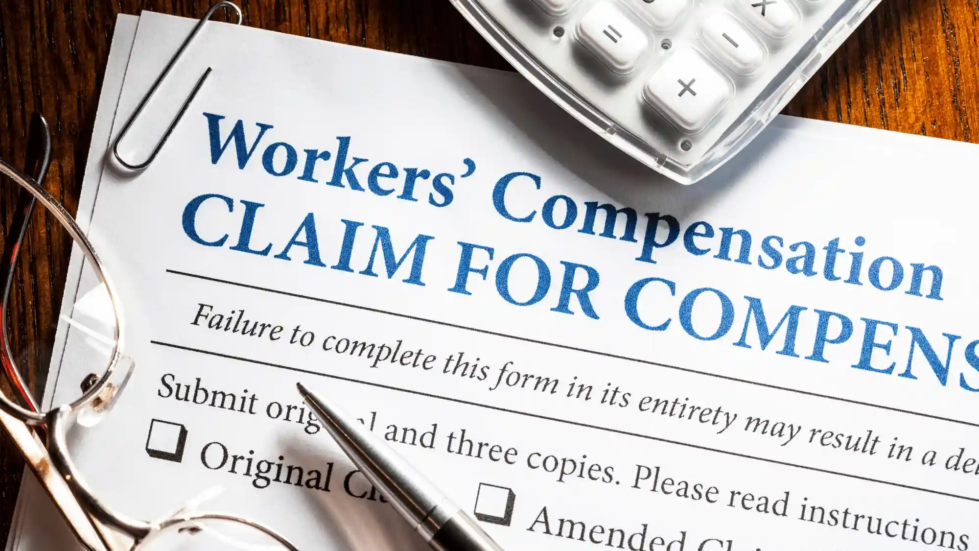 How Oregon Workers’ Comp Works Close-up of an Oregon workers’ compensation claim form with eyeglasses, a pen, and calculator representing the claims process and workplace injury benefits.