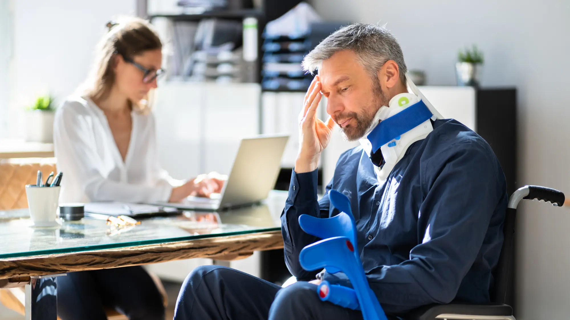 Workers’ Comp vs Disability in Oregon Injured worker wearing a neck brace and using crutches while discussing workers' compensation and disability benefits with an attorney.